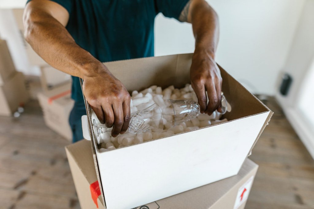 Hombre embalando objetos de cristal frágiles de manera cuidadosa en caja