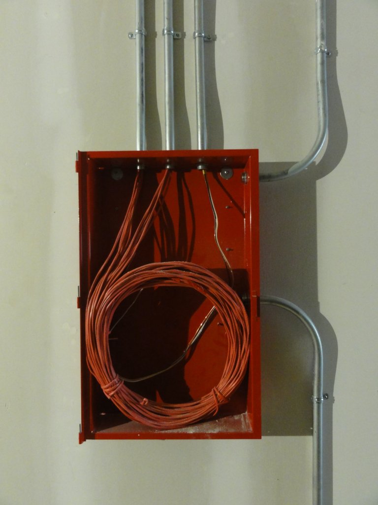 Caja de registo roja con tubos conduit sobre pared blanca instalaciones eléctricas