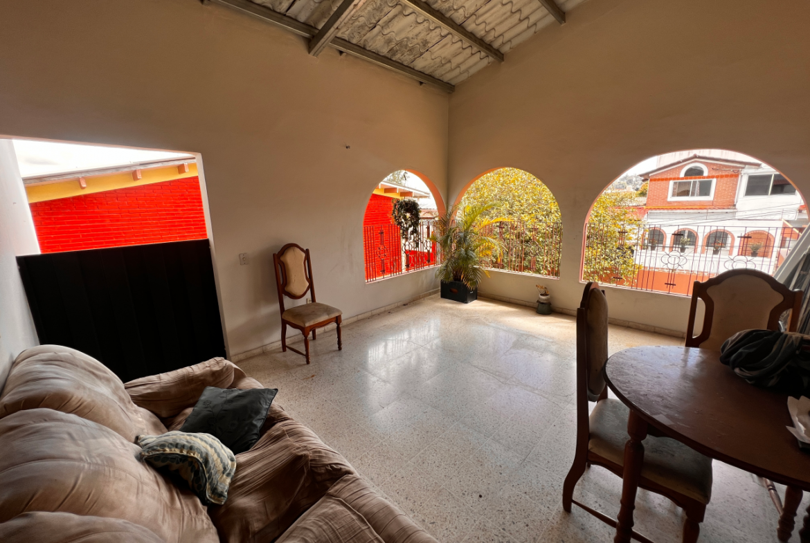 Terraza techada con un sofá grande, un comedor de madera de forma circular con 4 sillas y vista de la residencial Centroamérica.