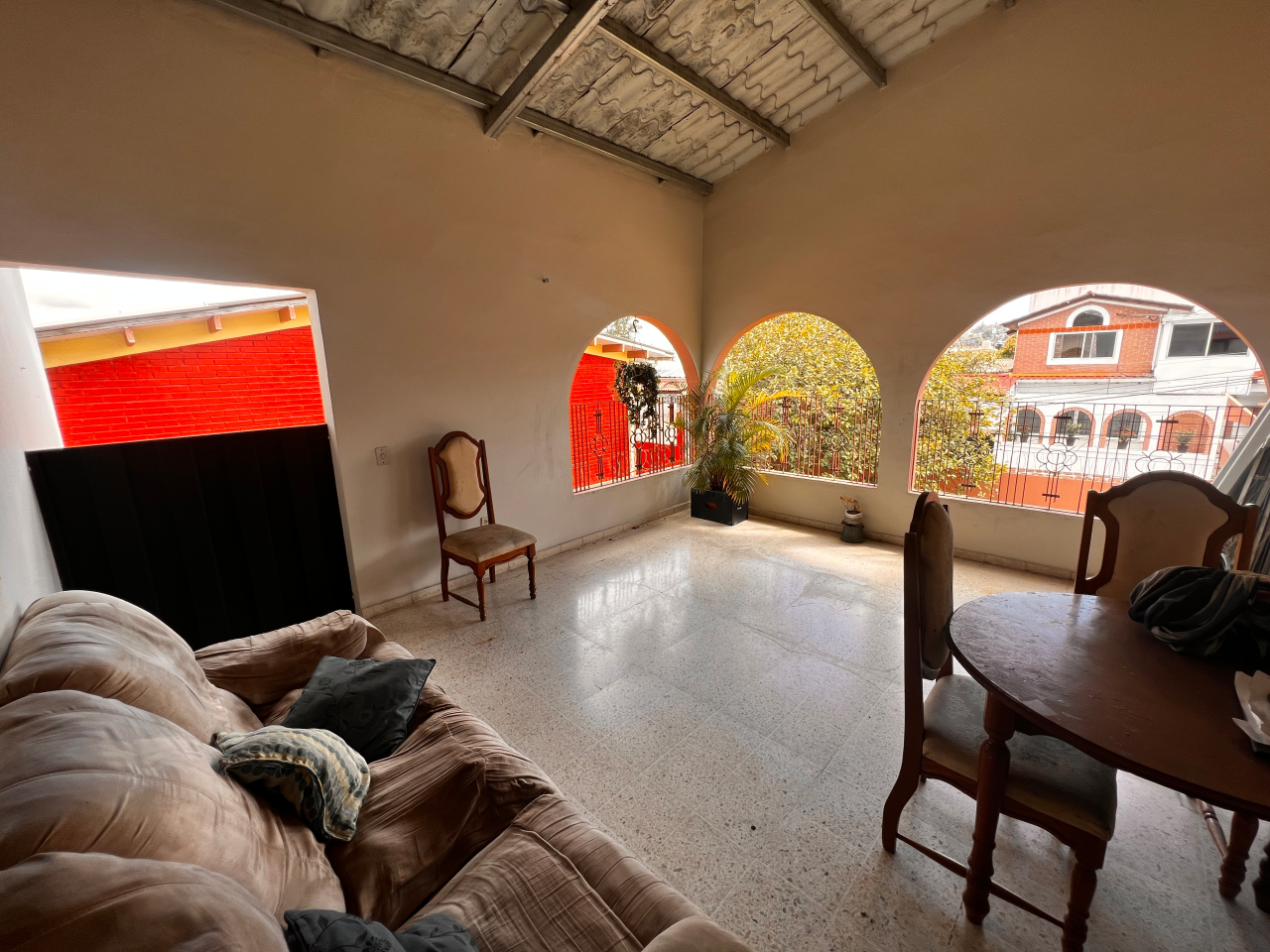 Terraza techada con un sofá grande, un comedor de madera de forma circular con 4 sillas y vista de la residencial Centroamérica.