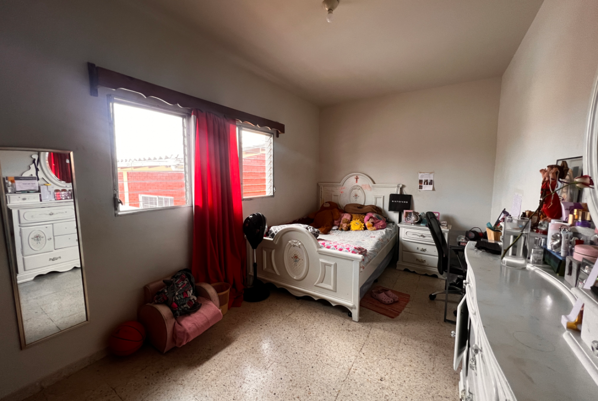 Dormitorio con paredes color blanco, una cómoda de madera color blanco y una ventana con vista de la residencial Centroamérica.