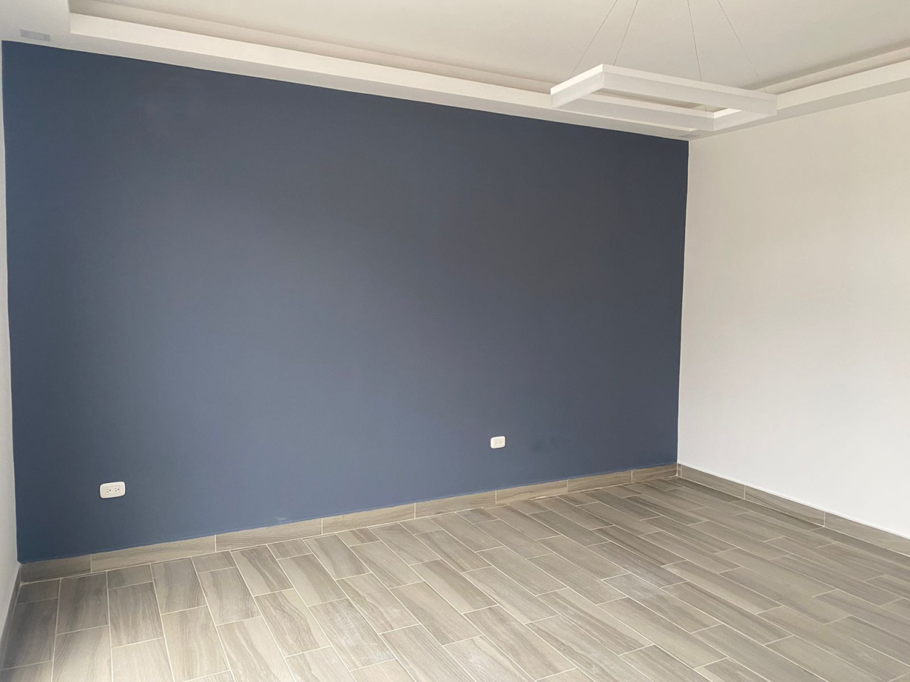 Habitación con acabados modernos color blanco, una pared color azul, y el piso de porcelanato tipo madera.