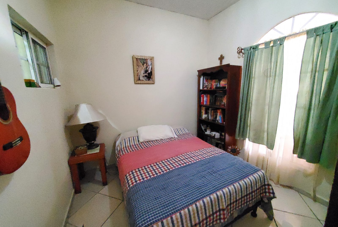 Habitación con una cama unipersonal, una lámpara sobre una mesita a un lado y al otro lado un mueble con varios libros en la Col. Modelo.