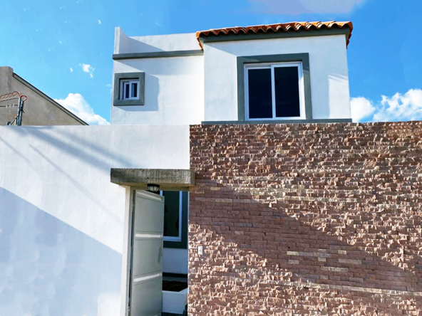 Fachada de casa ubicada en Res. Roble Oeste, es de color blanco y ladrio en el muro de enfrente, tiene 2 niveles y cuenta con un muro perimetral.