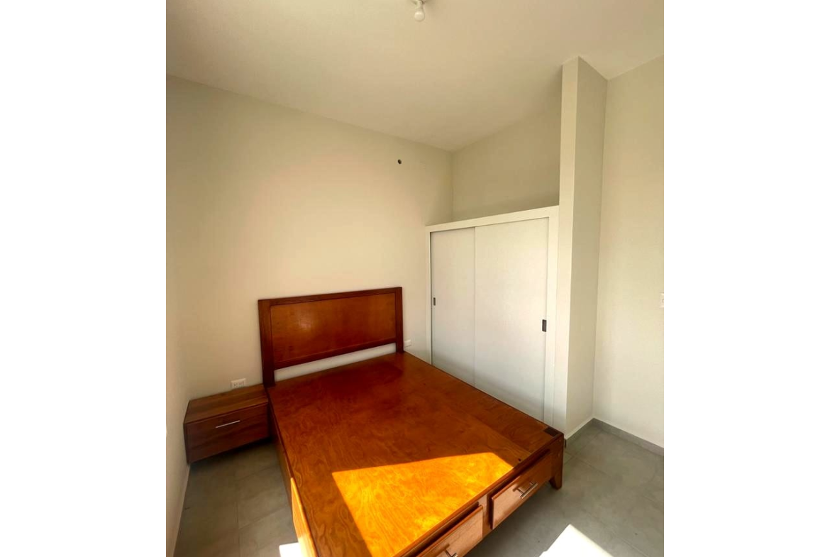 Habitación con cama de madera, closet color blanco y una mesa de noche al lado de la cama.