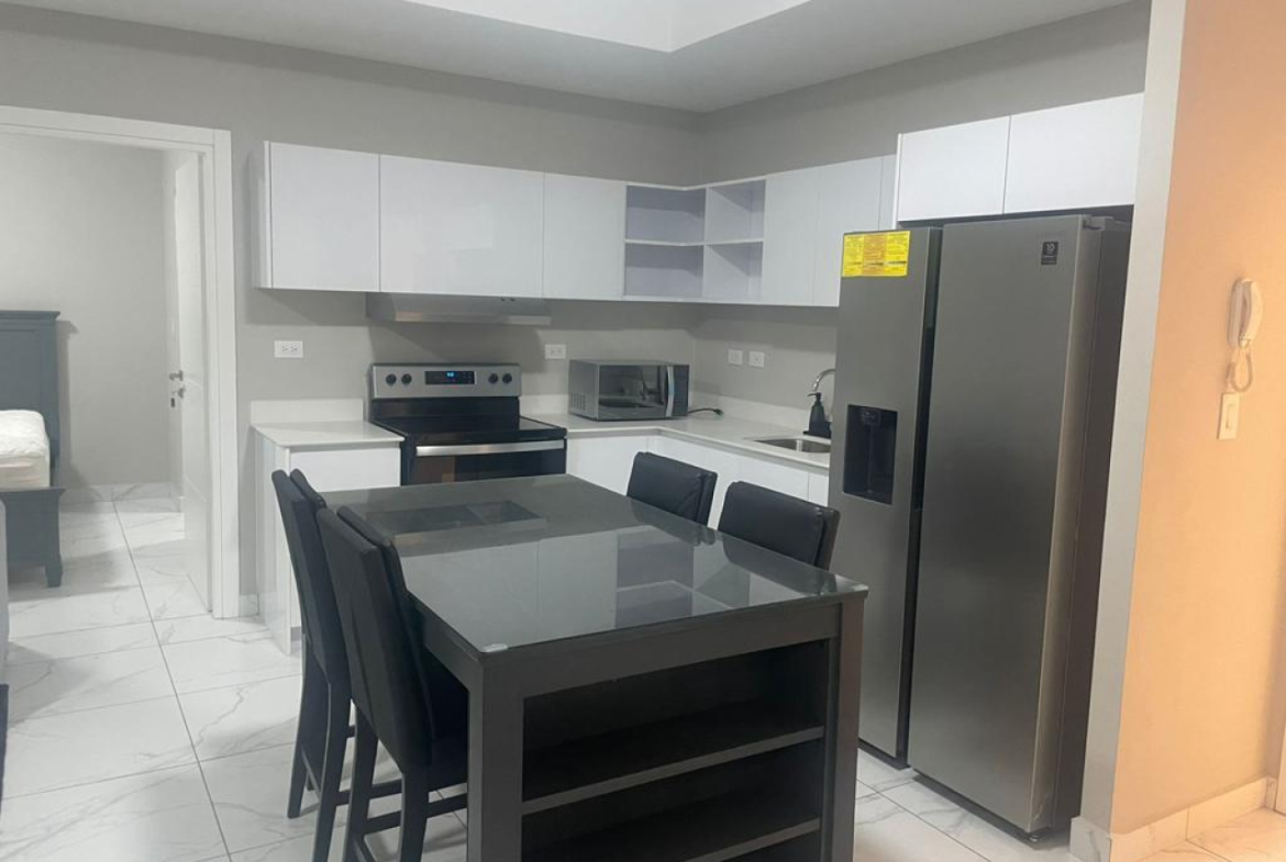Cocina del apartamento en torre nivo, comedor negro, muebles de cocina color blanco junto a refrigerador, estufa y microondas de acero.