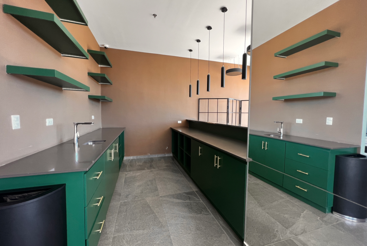 Área social de torre Agalta con muebles de cocina color verde y plancha de granito color negro, paredes color café claro, repisas y lámparas colgantes.