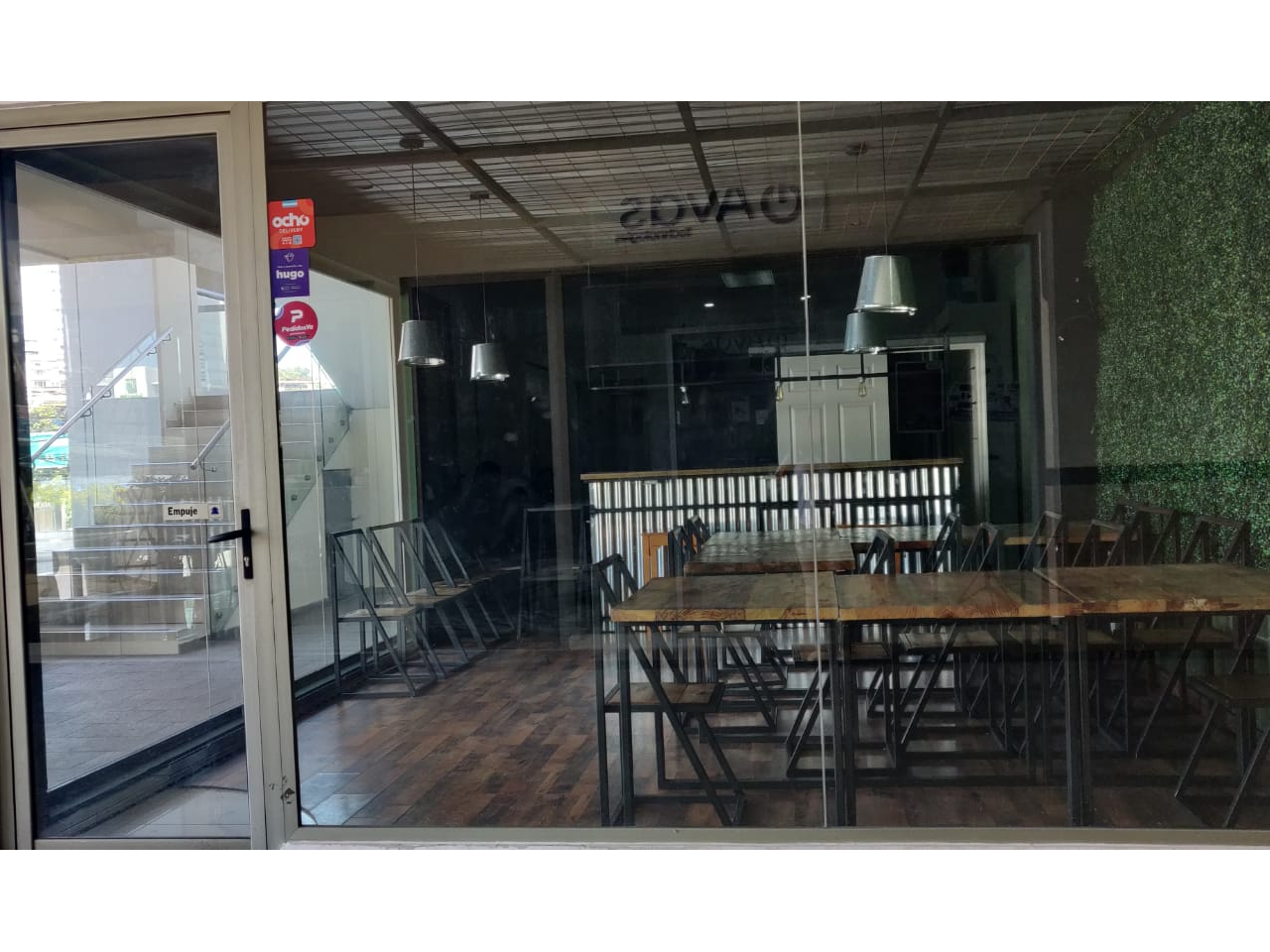 Local comercial para restaurante con división perimetral de vidrio de piso al techo una puerta, y muebles de restaurante dentro del local.