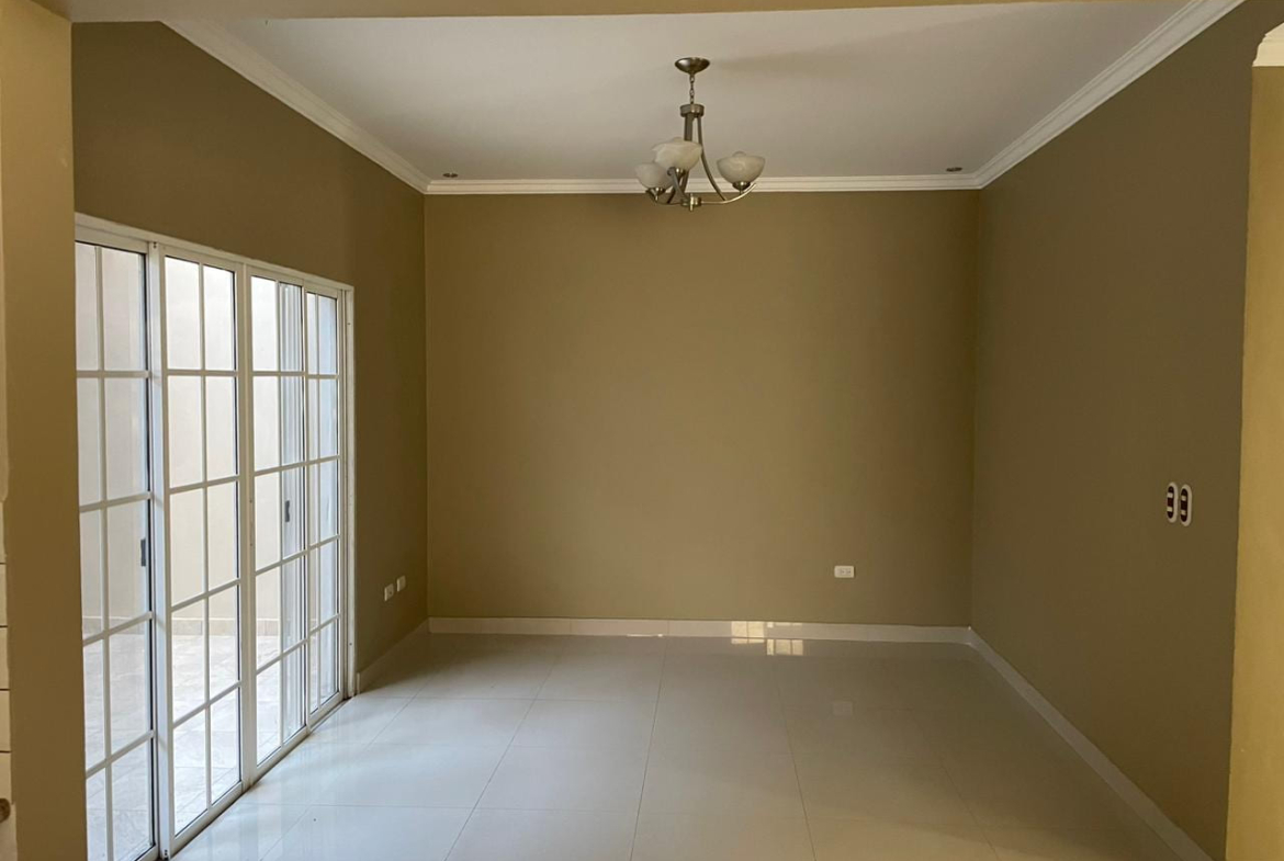 Sala de estar con piso porcelanato, pared color beige, techo tabla yeso y puerta corrediza con acceso al patio.