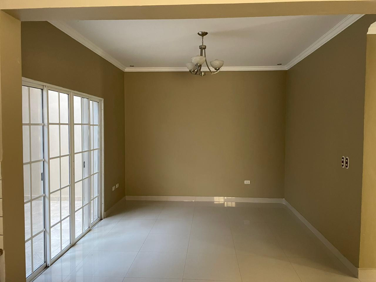 Sala de estar con piso porcelanato, pared color beige, techo tabla yeso y puerta corrediza con acceso al patio.