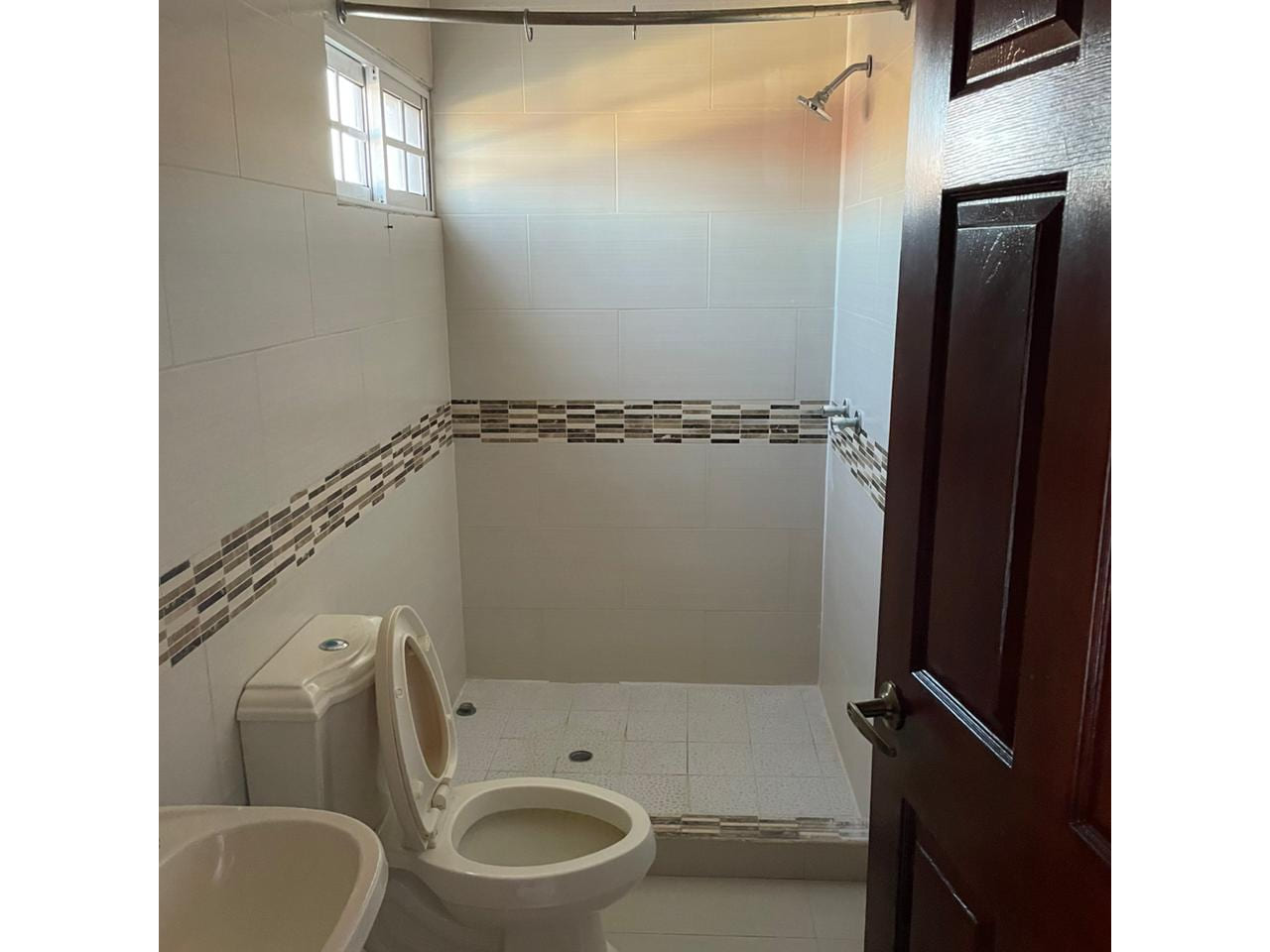 Baño completo, inodoro, piso porcelanato, pared color beige, techo tabla yeso, ducha con azulejos.