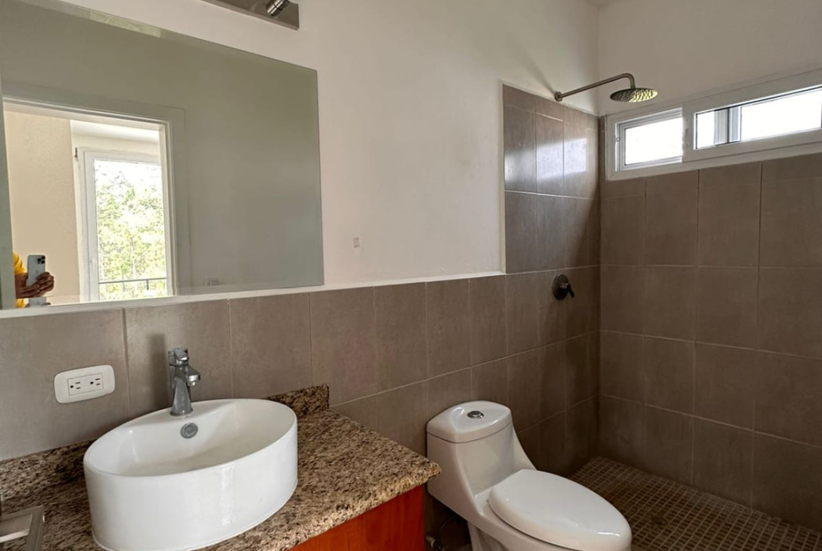 Amplio baño con regadera de suelo de cerámica, servicio, moderno lavamanos, con un espejo en frente e iluminación moderna.