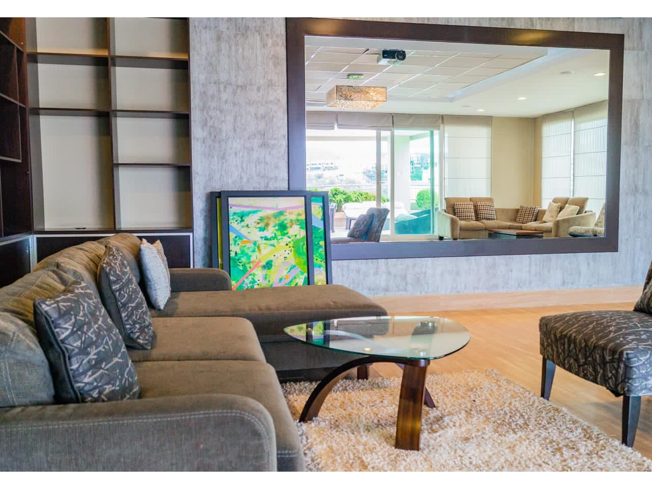 Área social lujosa con muebles de color café, amplio espejo, mesa de cristal con alfombra de peluche color claro.