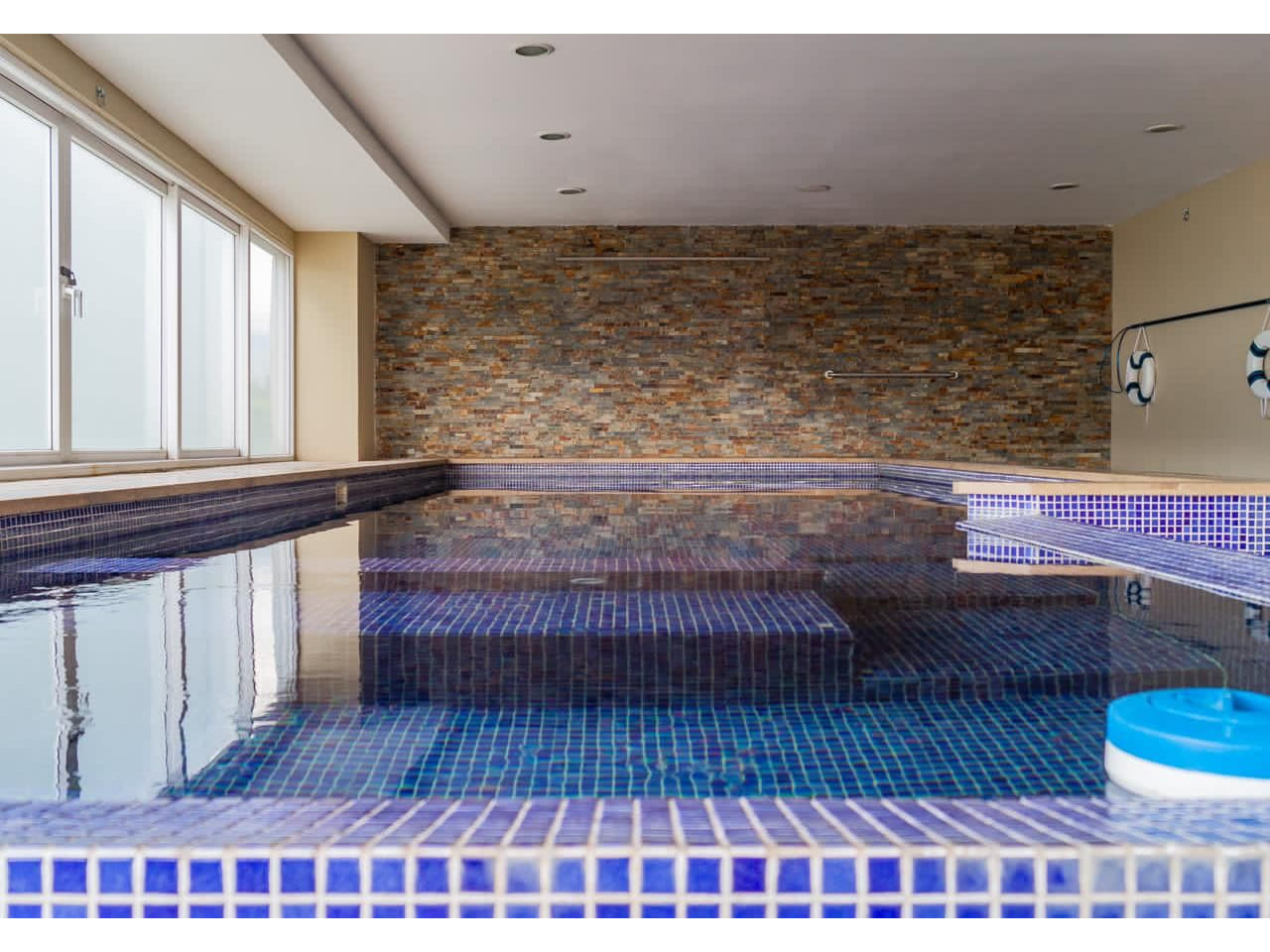 Área de piscina amplia, con ventanas que dan al exterior, paredes de color crema con acabados modernos.