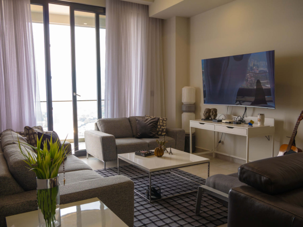 Sala de estar del apartamento en renta de torre aria, con muebles, mesa de centro, un televisor plasma y una ventana con cortinas larga.