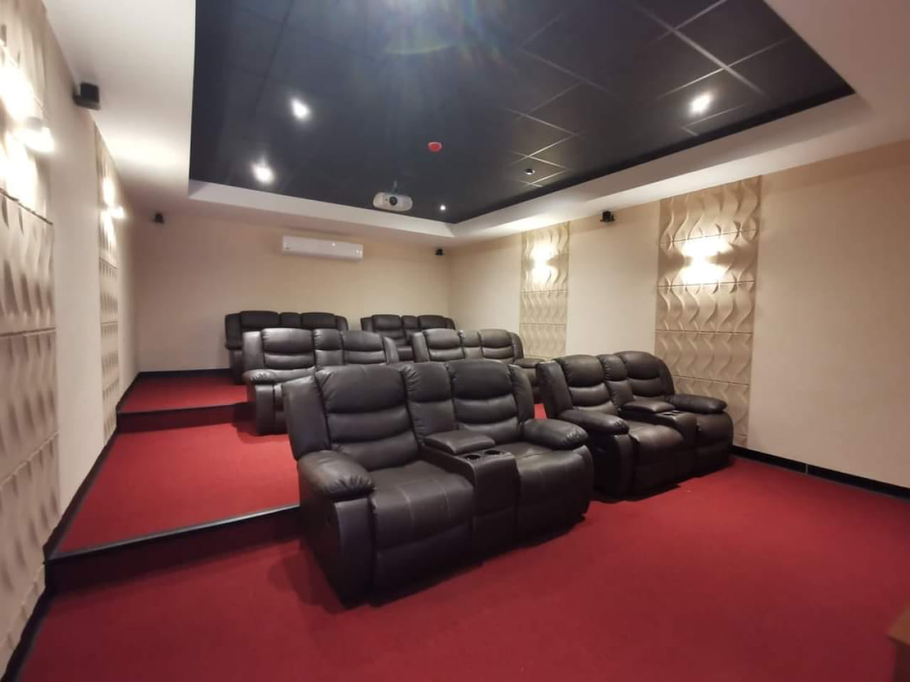 Área de cine, cuenta con suelo de alfombra roja, paredes de color blanco con material antiecos, sillones de color café.