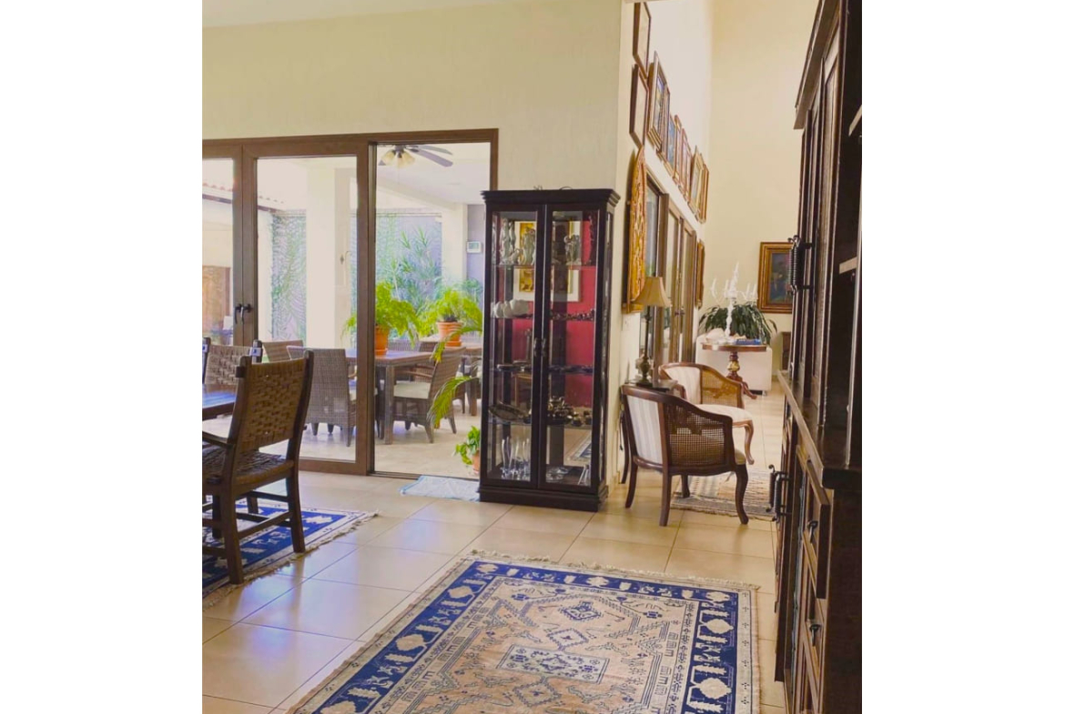 Pasillos de la casa en venta , con alfombla de color azul, mueble de madera con adornos de ceramica, junto al pasillo de la sala de estar y a la puerta del patio trasero.