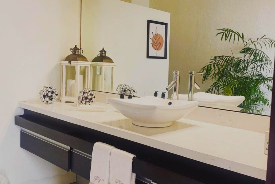 Baños completo con lavamanos,una plancha de granito color blanco, muebles de madera color negro y un espejo grande.