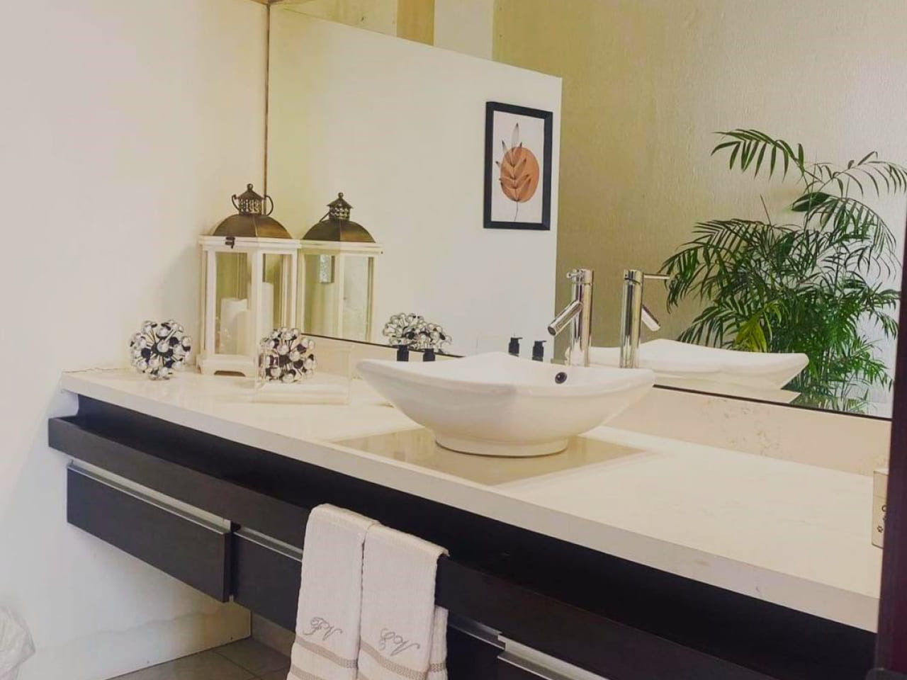 Baños completo con lavamanos,una plancha de granito color blanco, muebles de madera color negro y un espejo grande.