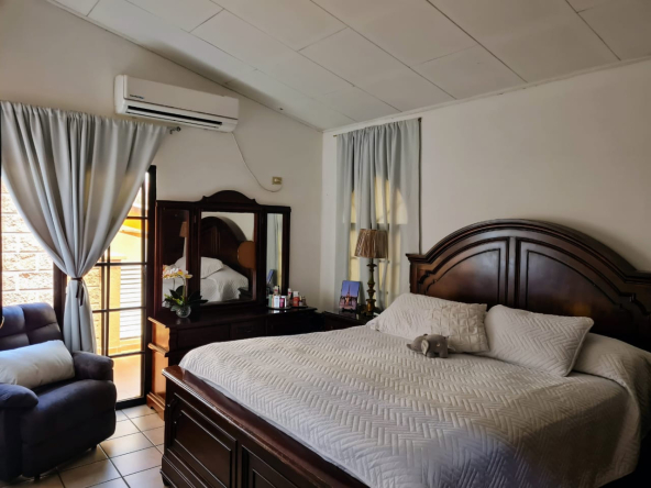Habitación de casa en venta en Las hadas con una cama matrimonial, espejo vertical junto a una silla acolchonada color blanco.