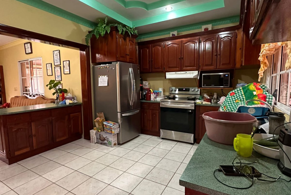 Area de cocina, con paredes de color amarillo suave, suelo de ceramica color blanco, muebles de color cafe barnizados, con area de lavado y espacio para colocar linea blanca.