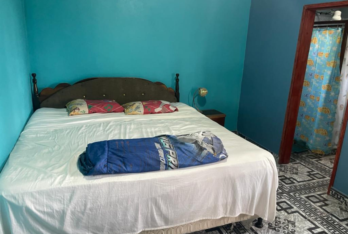 Habitación con cama matrimonial, televisión, piso de cerámica, techo de tabla yeso, pared color azul y baño privado.