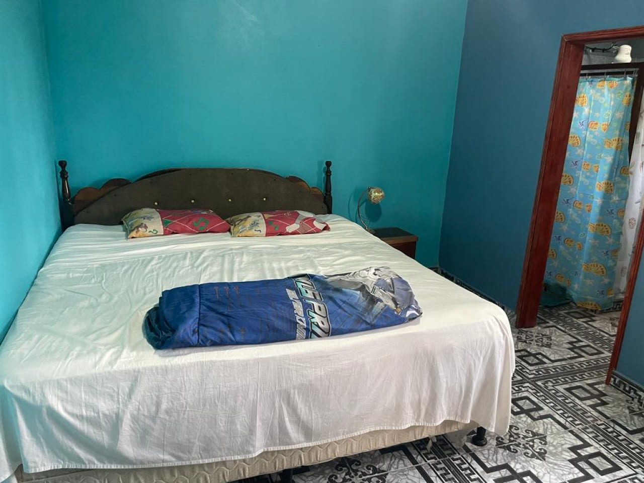 Habitación con cama matrimonial, televisión, piso de cerámica, techo de tabla yeso, pared color azul y baño privado.