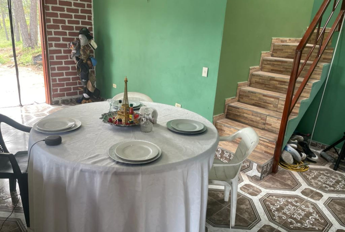 Sala de comedor con pared color verde, piso de cerámica, escaleras con acceso al 2 nivel y una puerta corrediza al patio trasero.