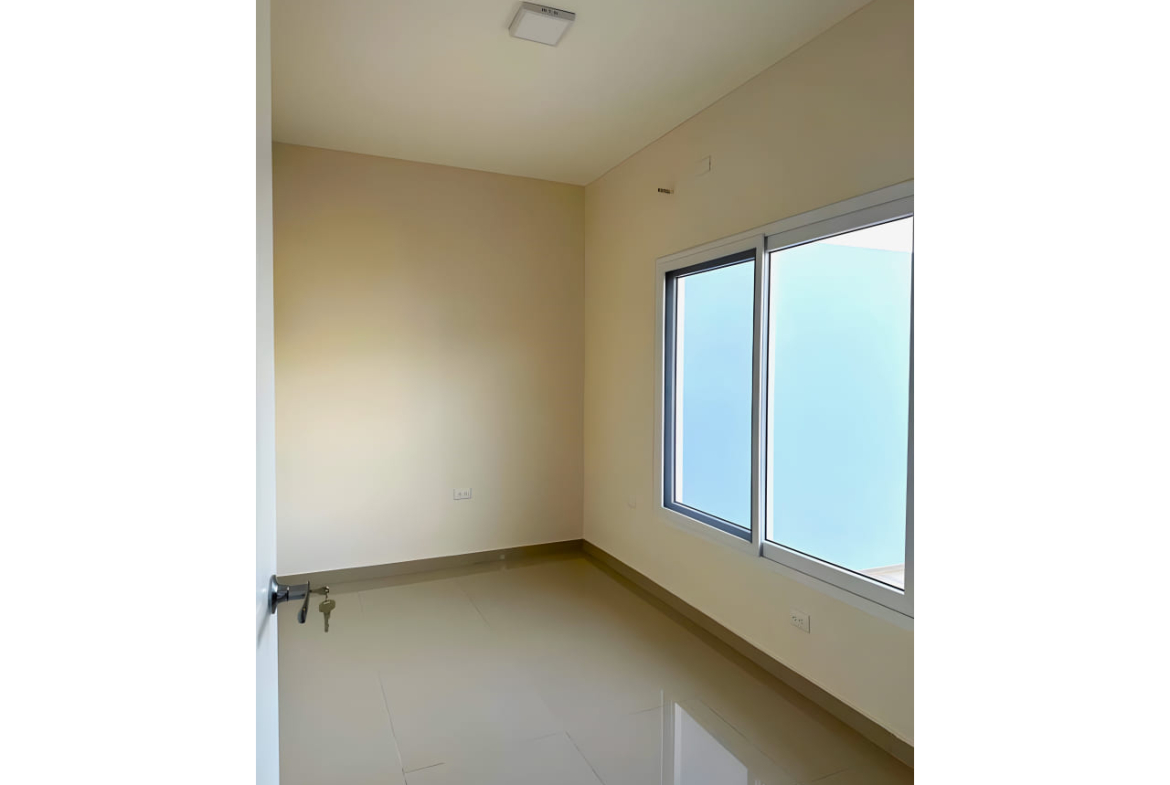 Amplia habitación ded paredes color blanco con suelo de porcelanato cuenta con closet de color chocolate, puerta de color blanca y una ventana que brinda iluminación calida a la habitación.