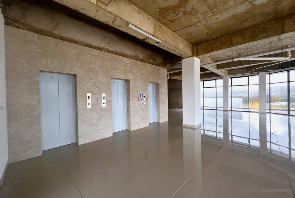 Área de tres asensores, con puertas de color gris claro, mas paredes en obra gris, una zona perfecta para que tus empleados accesadan a las intalaciones, con una amplia ventana en el fondo qjue brinda iluminación natural.