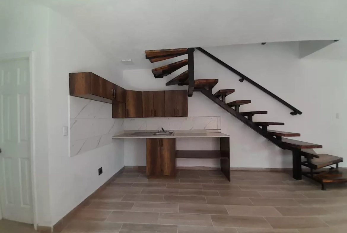 Área de cocina con muebles de madera y lavandería, con acceso a espacio para comedor y sala, con acceso a escaleras de madera.