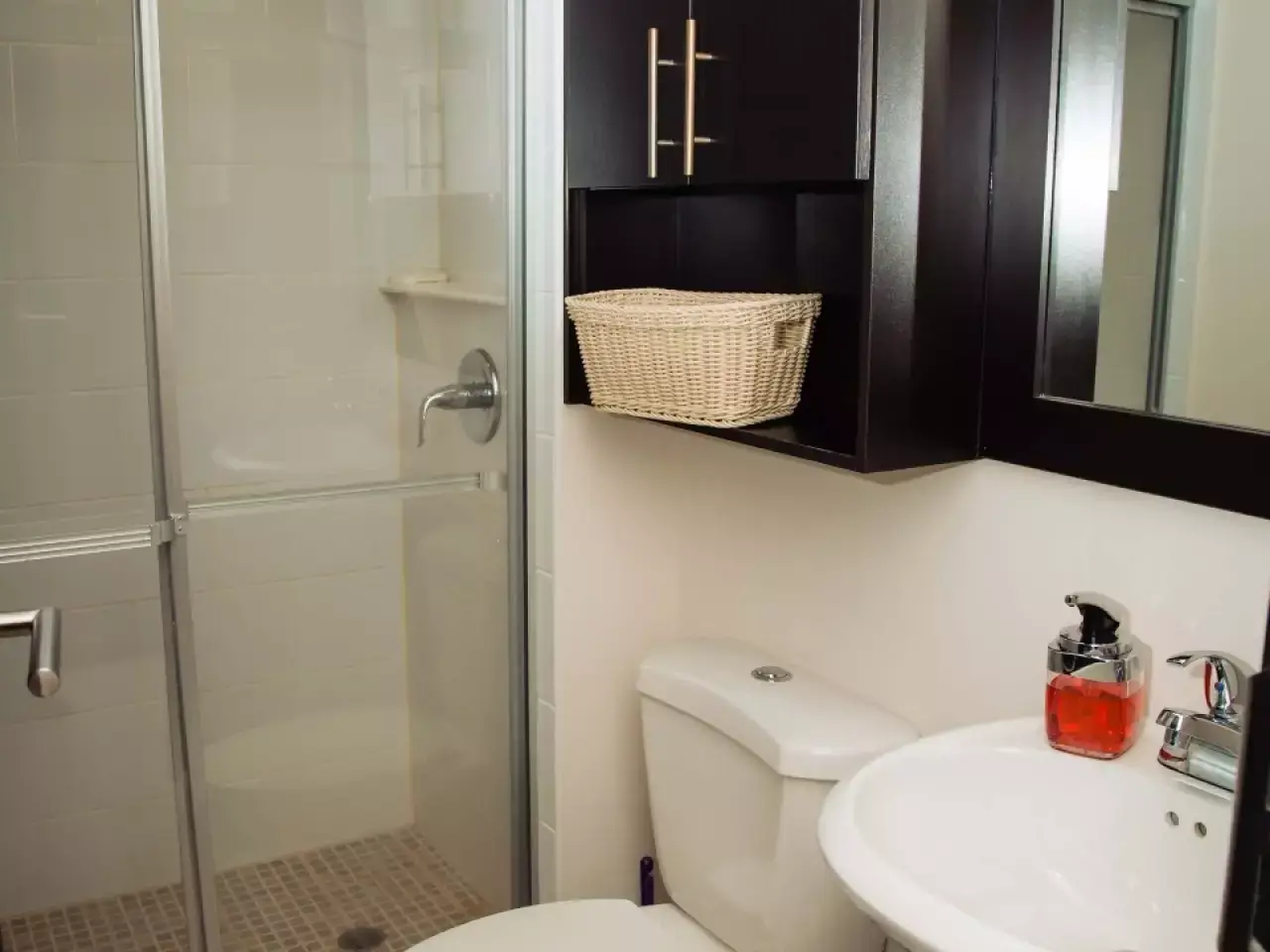 baño completo con regadera con suelo de ceramica, retrete y lavamanos de color blanco a juego y un mueble de madera oscura para guardas objetos de higiene personal