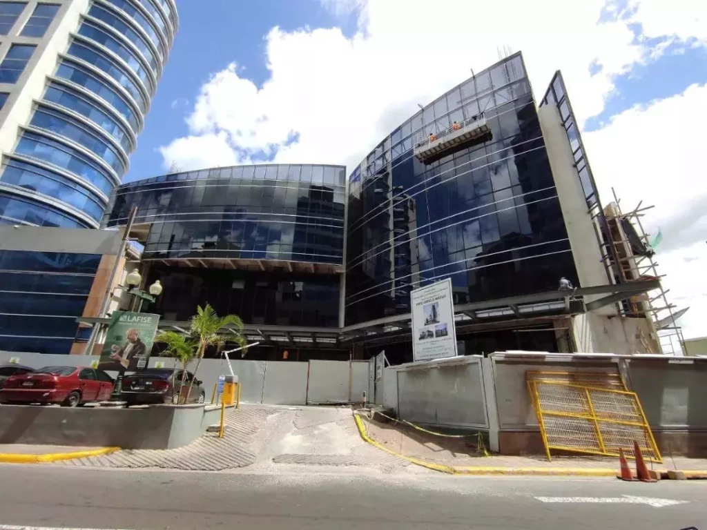Edificio vertis en pase los proceres, con varios niveles de oficinas, estacionamiento enfrente, de día con cielo azul.