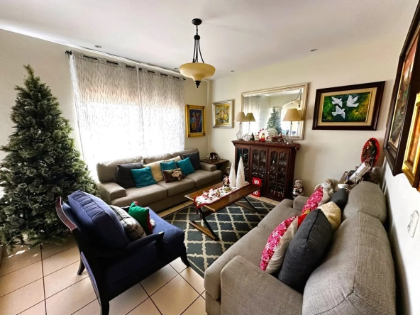 Sala de estar principal cuenta con dos hermsos sillones de color gris decorados concojines de color azul y rojo, el árbol de navidad y las paredes estan decoradas con diferentes cuadros.